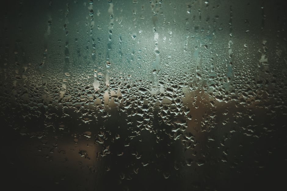 Close-up of raindrops on a glass window with a dark and moody ambiance.