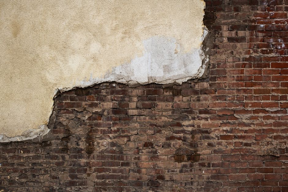Close-up of an old brick wall with peeling plaster, showcasing texture and decay.