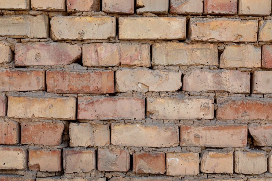 A close-up view of a rustic red brick wall with an uneven and textured surface.