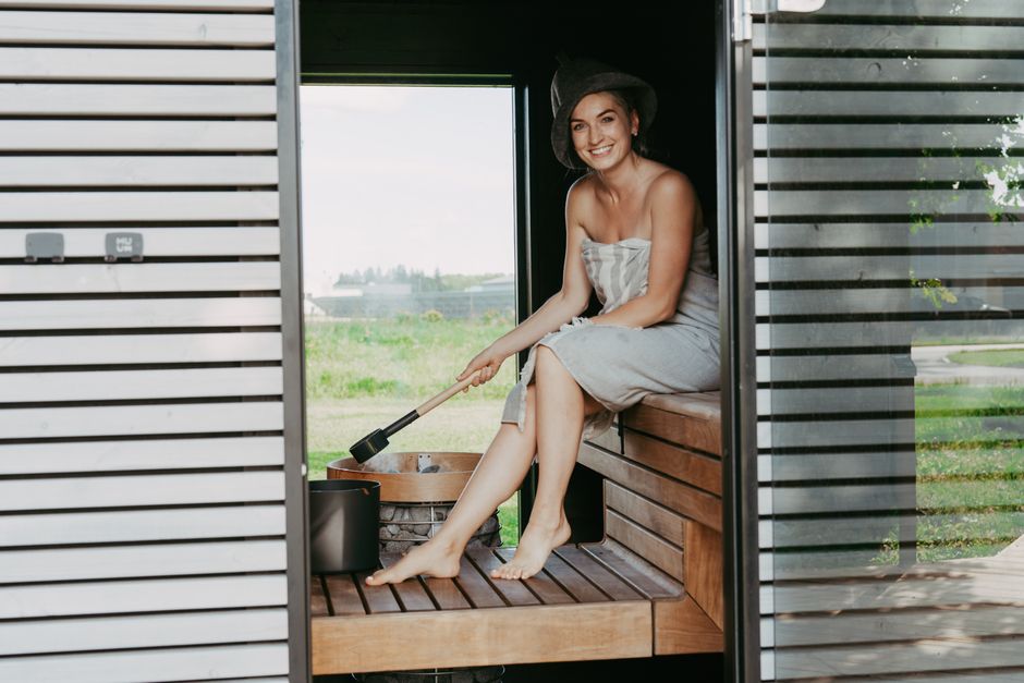 A woman enjoys a relaxing moment in a Nordic-style sauna, sitting and smiling.