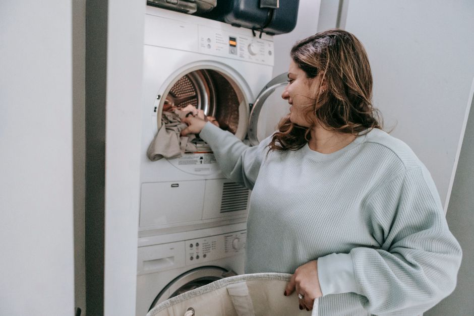 Glad female in casual wear loading dirt clothes in modern white washing machine while sitting in bathroom during household routine