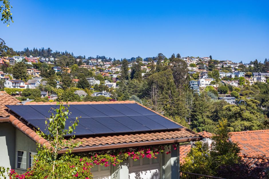 Solar panels on a suburban home, surrounded by lush greenery and a sunny blue sky.